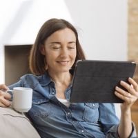 Woman sitting on couch with a cup of tea looking at tablet