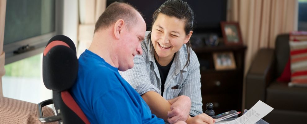 A young female carer helps a disabled man with reading